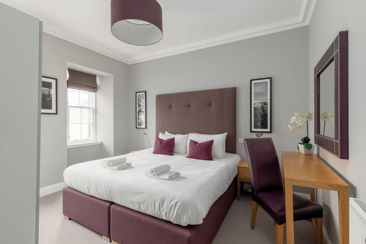 A neatly arranged bedroom with a large bed, a wooden desk, and a chair.