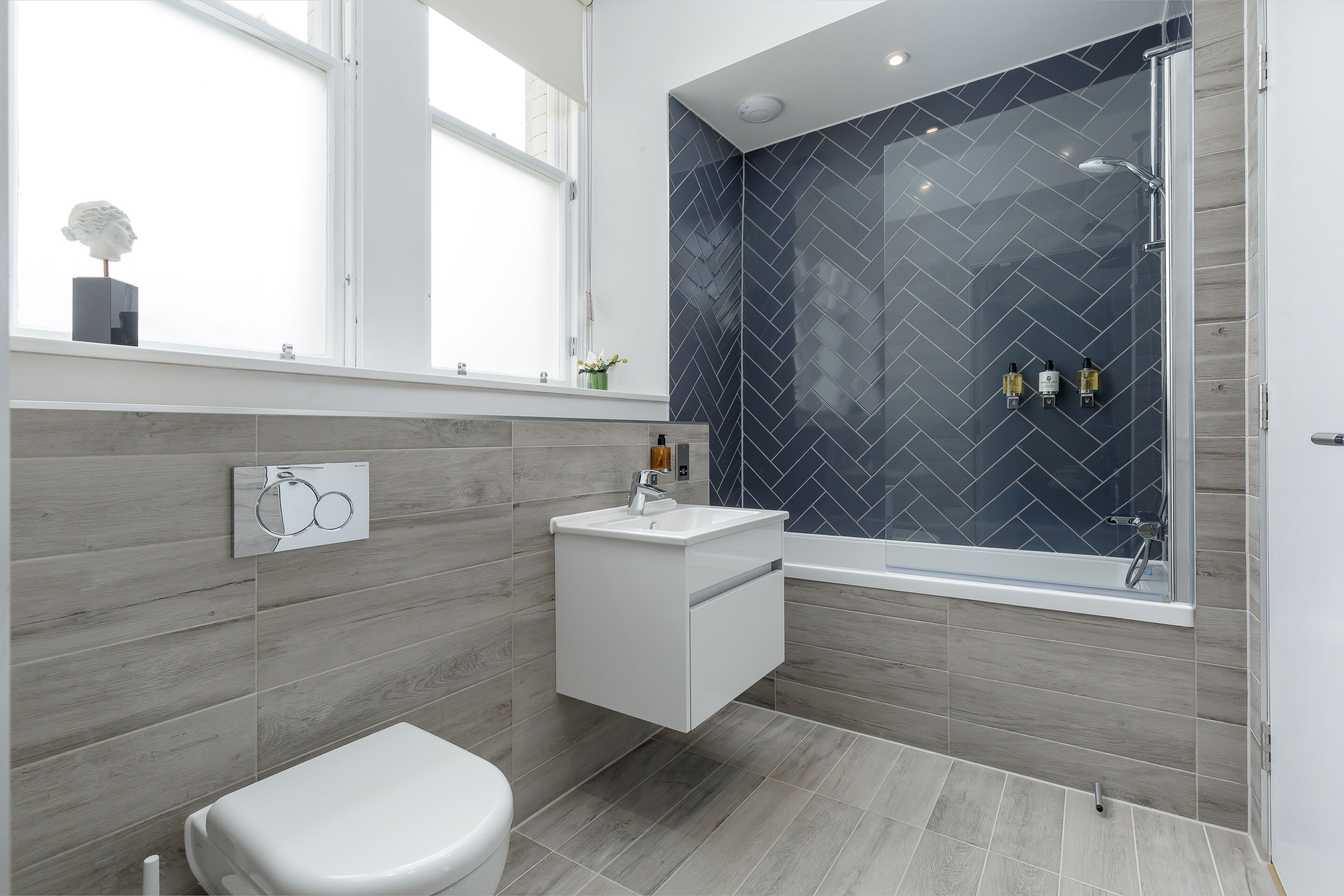 Un baño moderno con inodoro independiente, lavamanos blanco y ducha con mampara de vidrio.