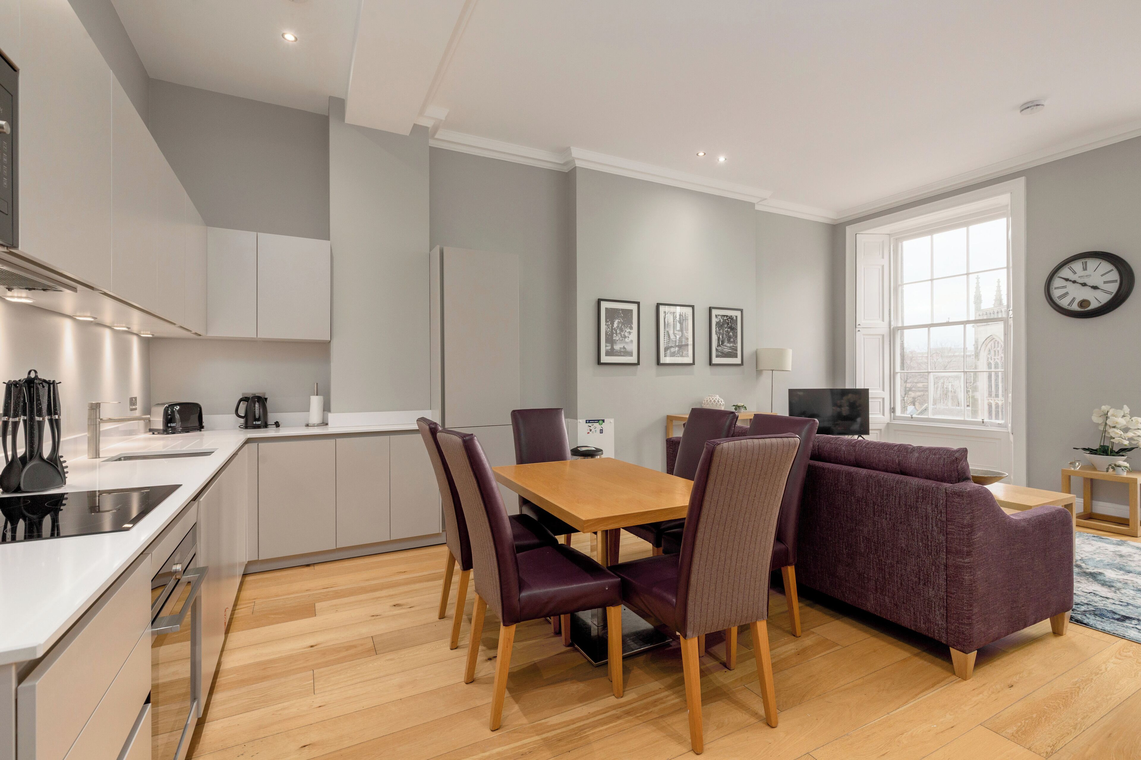 A modern kitchen with white cabinets, a wooden dining table, and purple chairs.