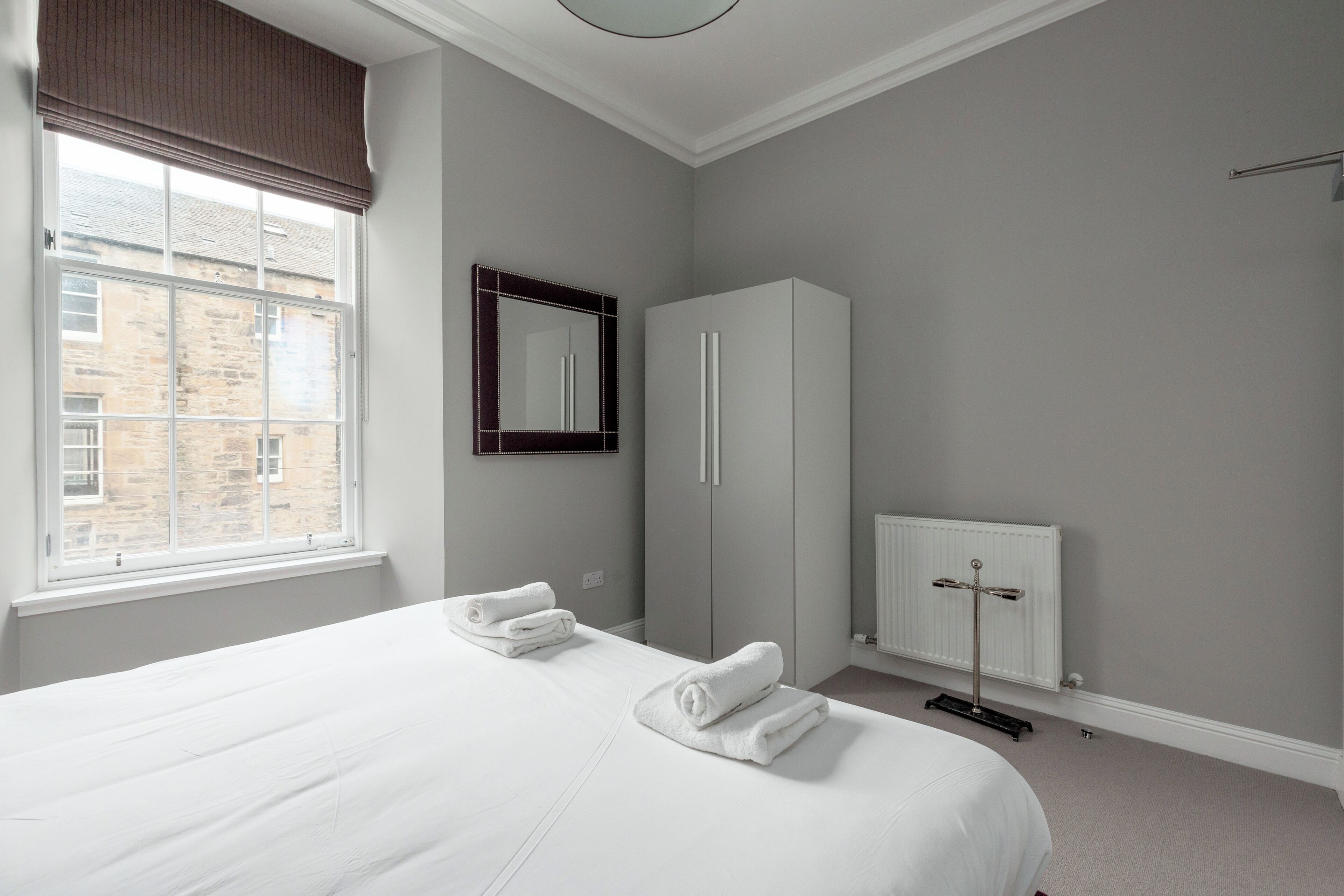 Une chambre d’hôtel avec un grand lit, une armoire, un radiateur et une fenêtre donnant sur un immeuble.