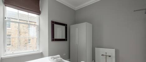 Une chambre d’hôtel avec un grand lit, une armoire, un radiateur et une fenêtre donnant sur un immeuble.