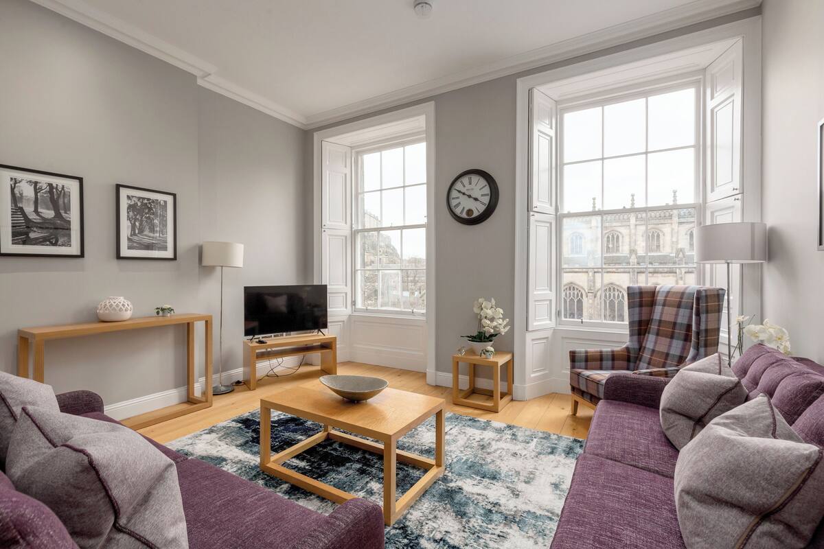 A living room with a sofa, coffee table, TV, and a view of a building through large windows.