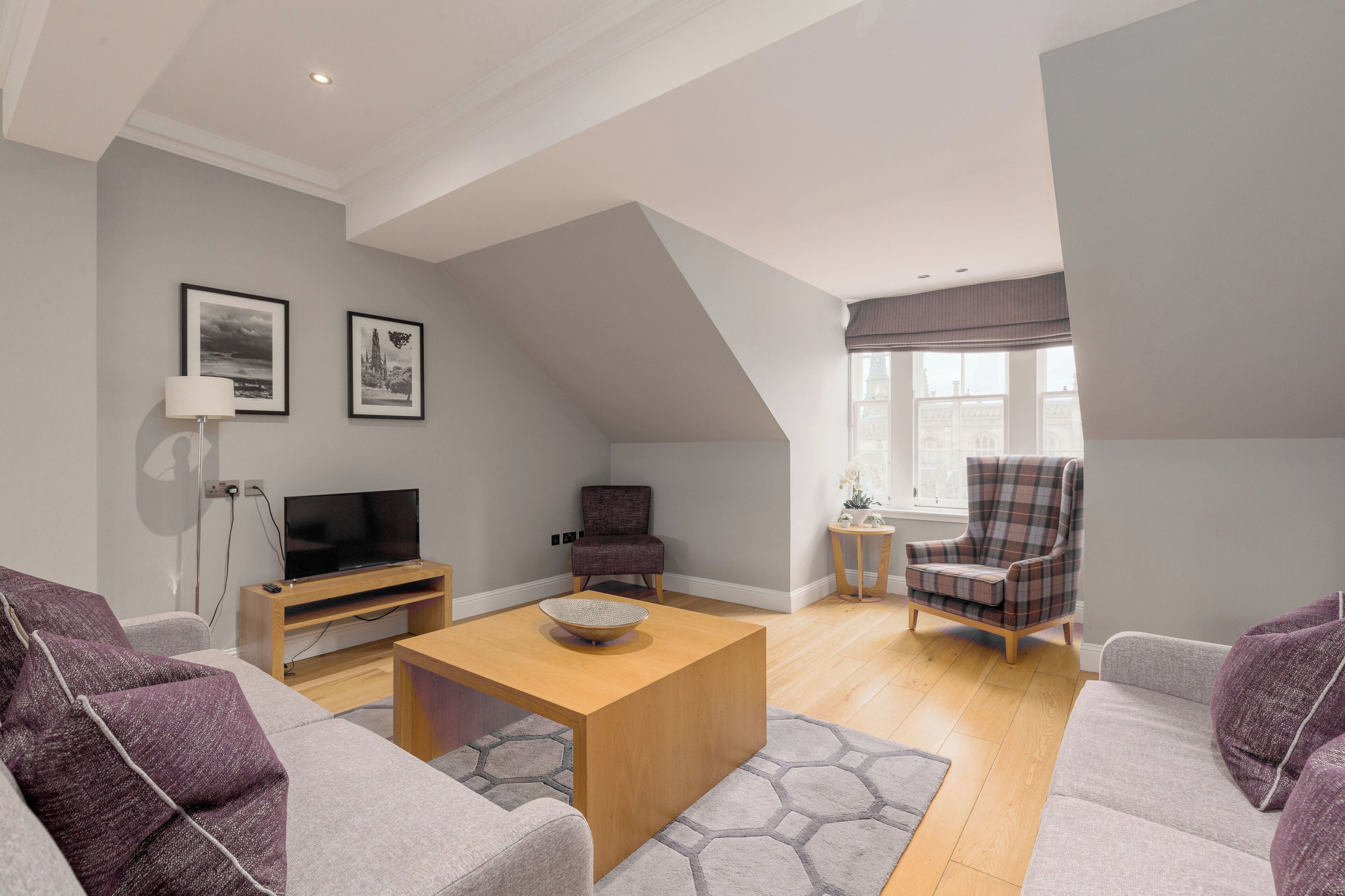 A modern living room with a television, seating, and artwork on the walls.