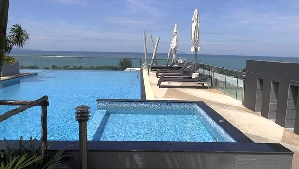 A swimming pool with lounge chairs and umbrellas, overlooking a body of water. - The Gallery Jomtien Beach Pattaya Condo By Dome (Pattaya)