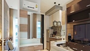 A modern kitchen with a built-in stove, a large flat-screen TV, and a dining area with a white table and chairs. - The Gallery Jomtien Beach Pattaya Condo By Dome (Pattaya)
