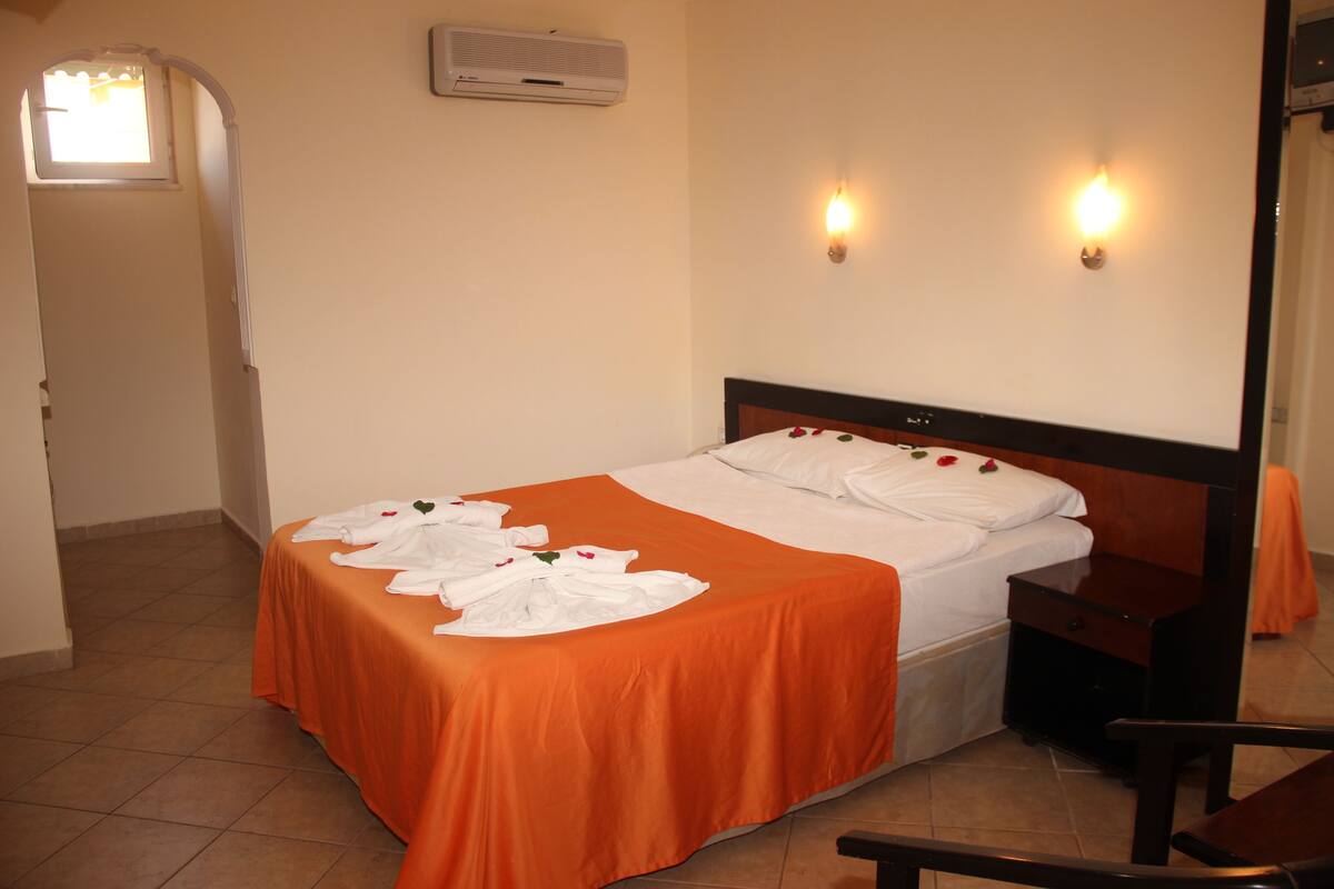 Una habitación de hotel con cama, aire acondicionado, dos luces fijadas a la pared y una mesita de noche de madera.