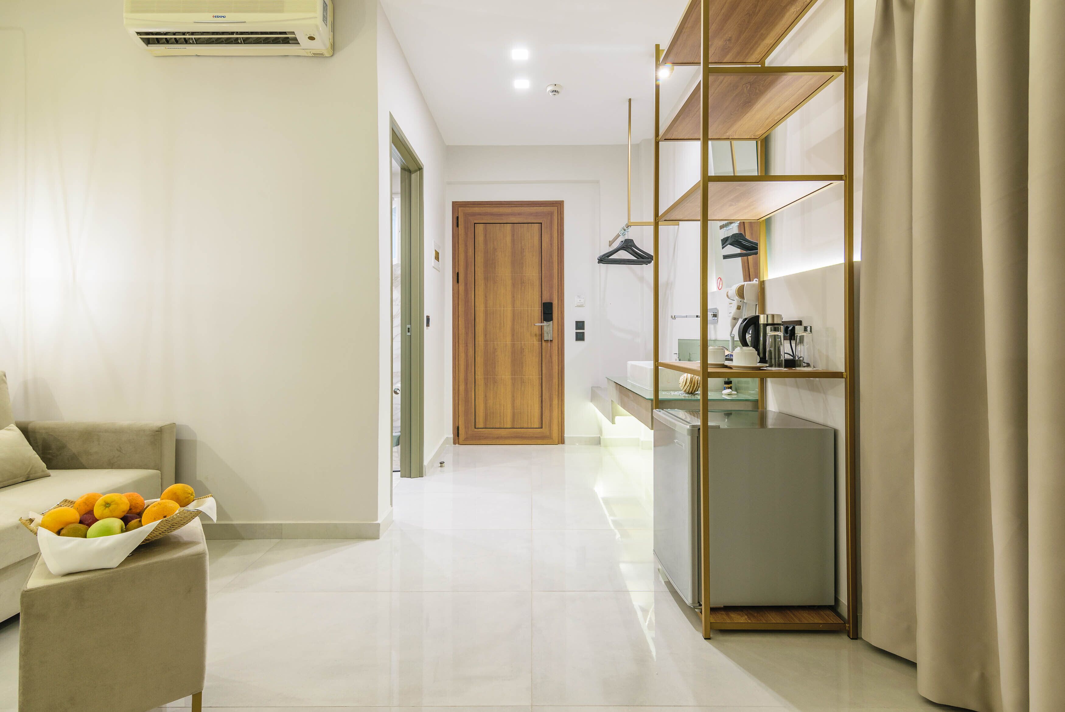 A modern hotel room with a sofa, a fruit bowl, a wooden door, and a kitchen area with a coffee machine.