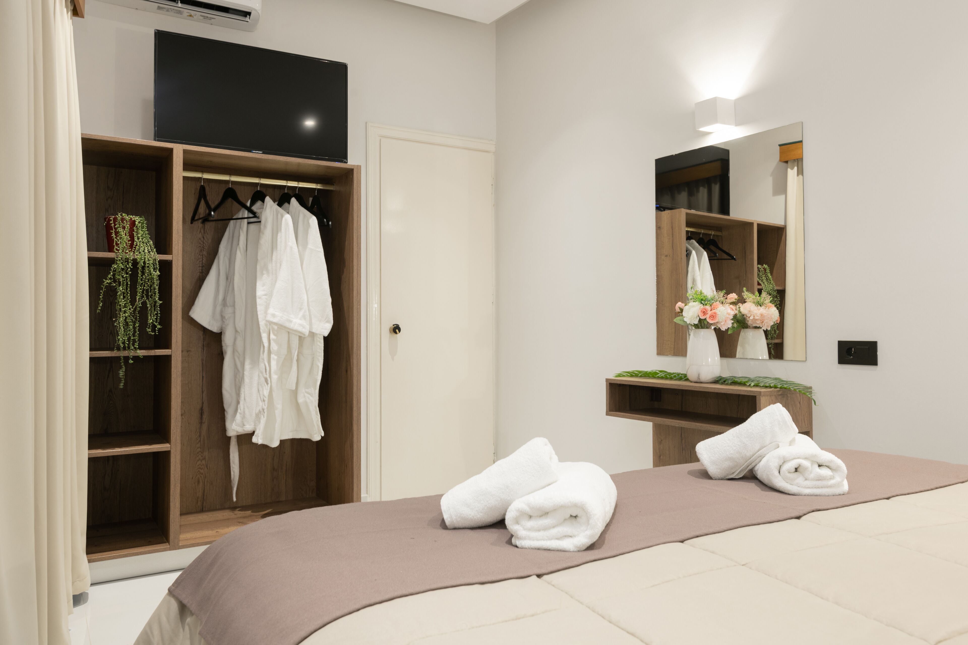 A bedroom with a bed, a wardrobe, a mirror, and a TV.