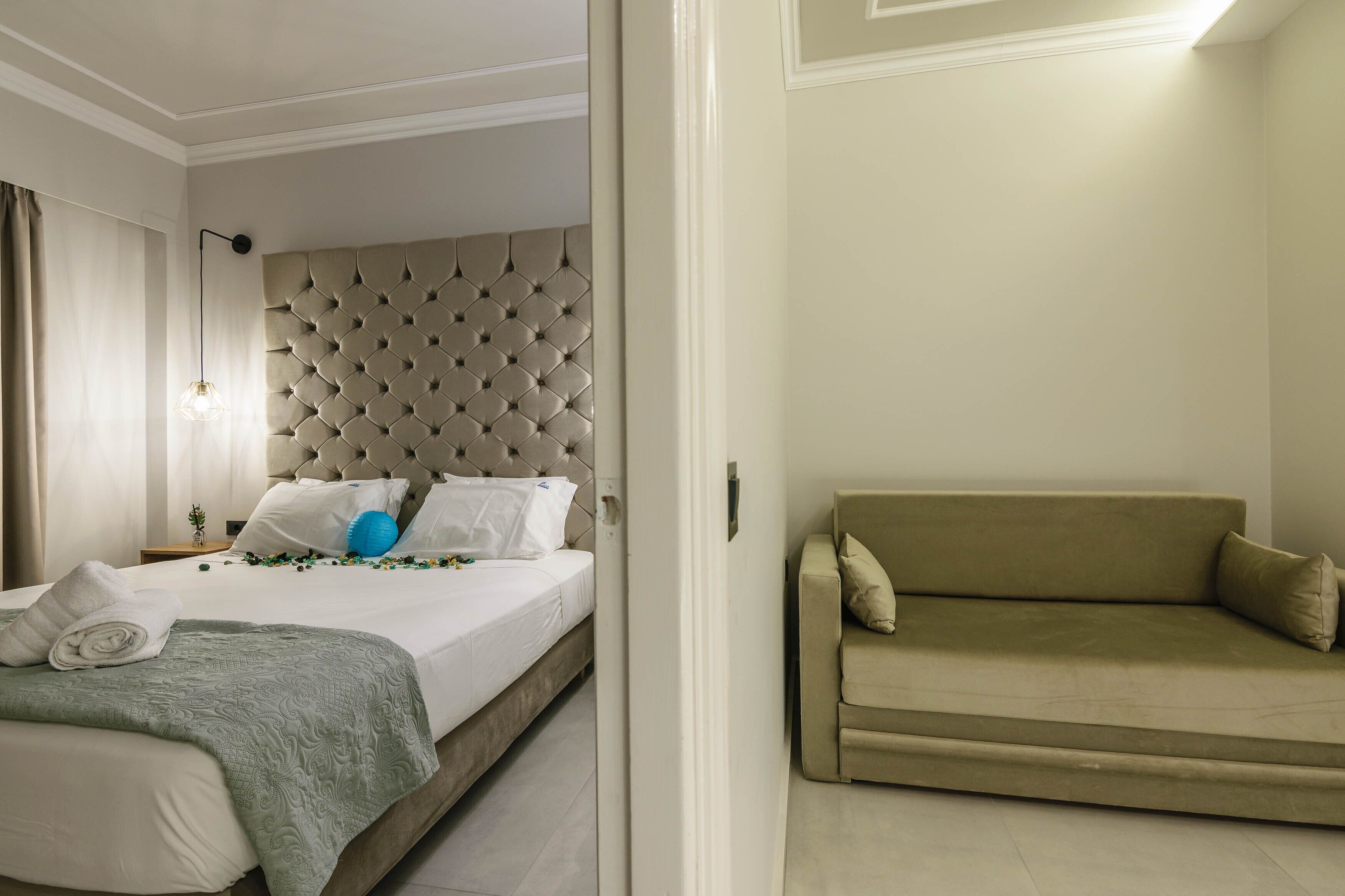 A hotel room with a bed, a headboard, a sofa, and a nightstand.