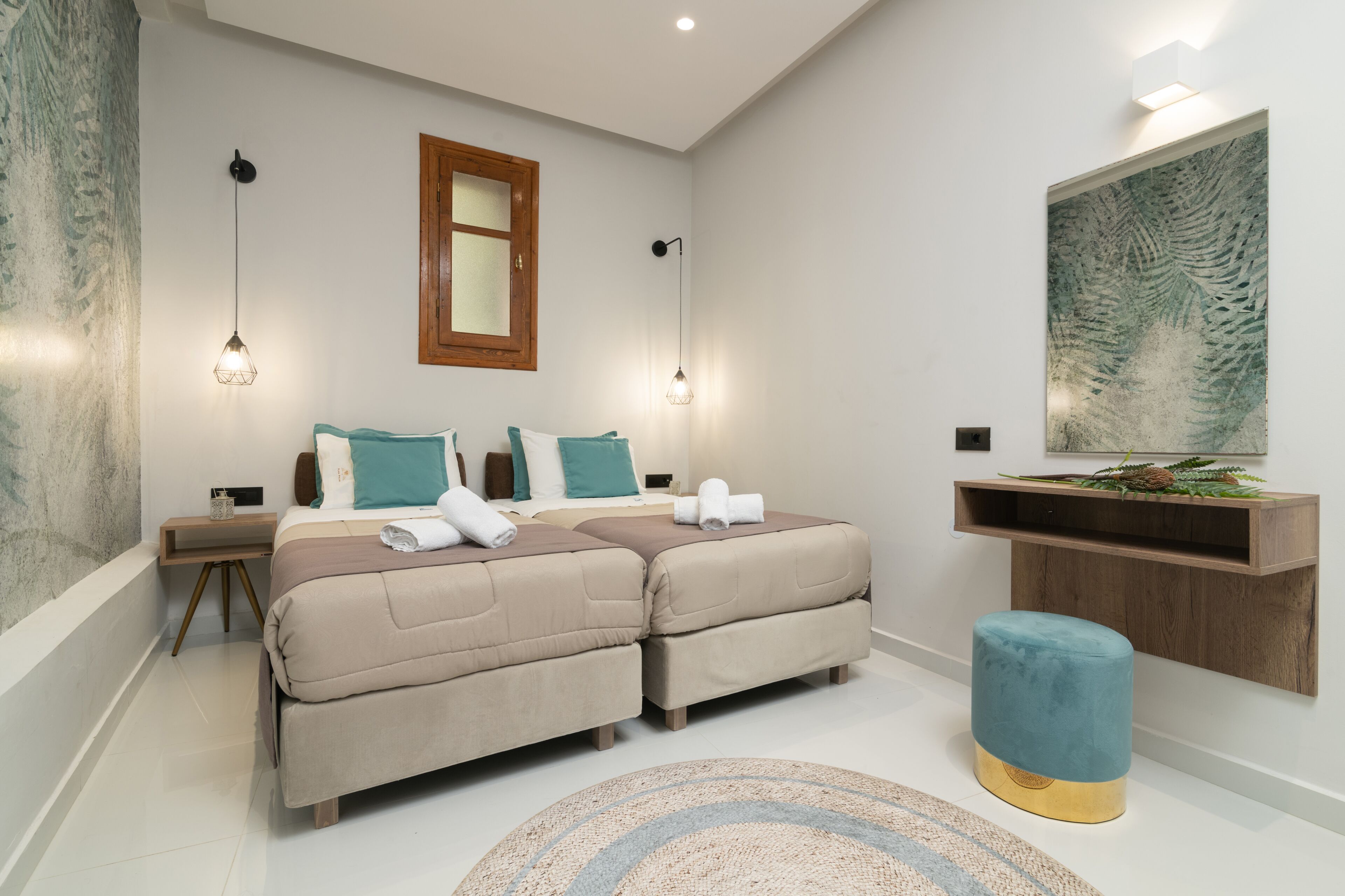 A modern bedroom with a double bed, bedside tables, a nightstand, a blue ottoman, a wooden shelf, and a large artwork on the wall.