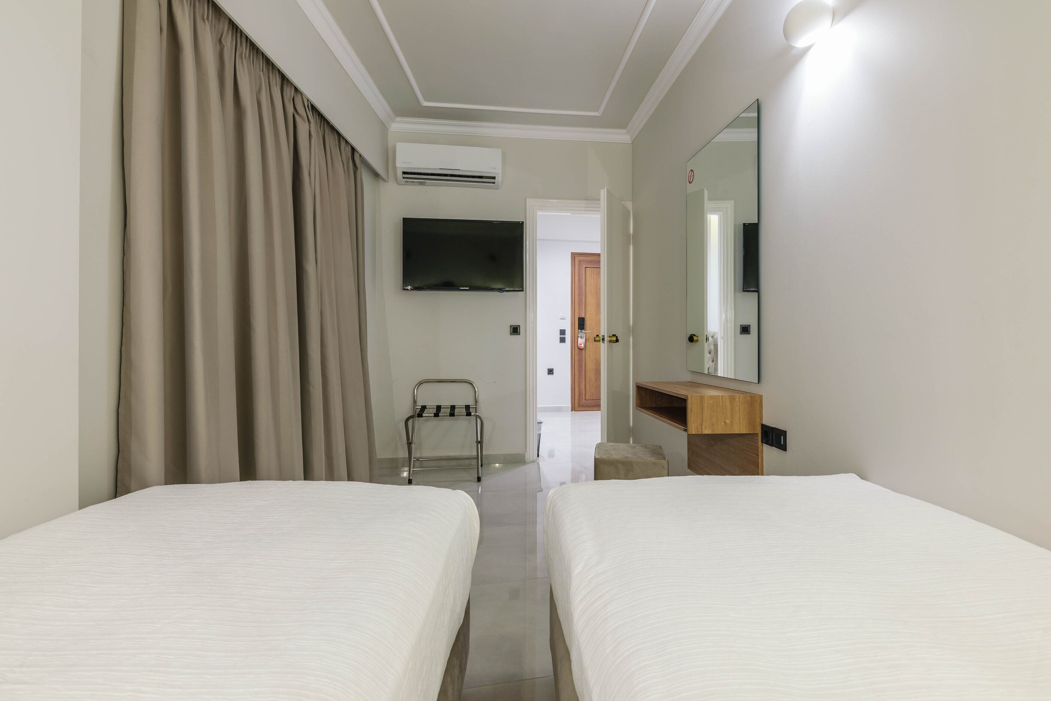 Habitación de hotel con dos camas, televisión, espejo y vestidor.