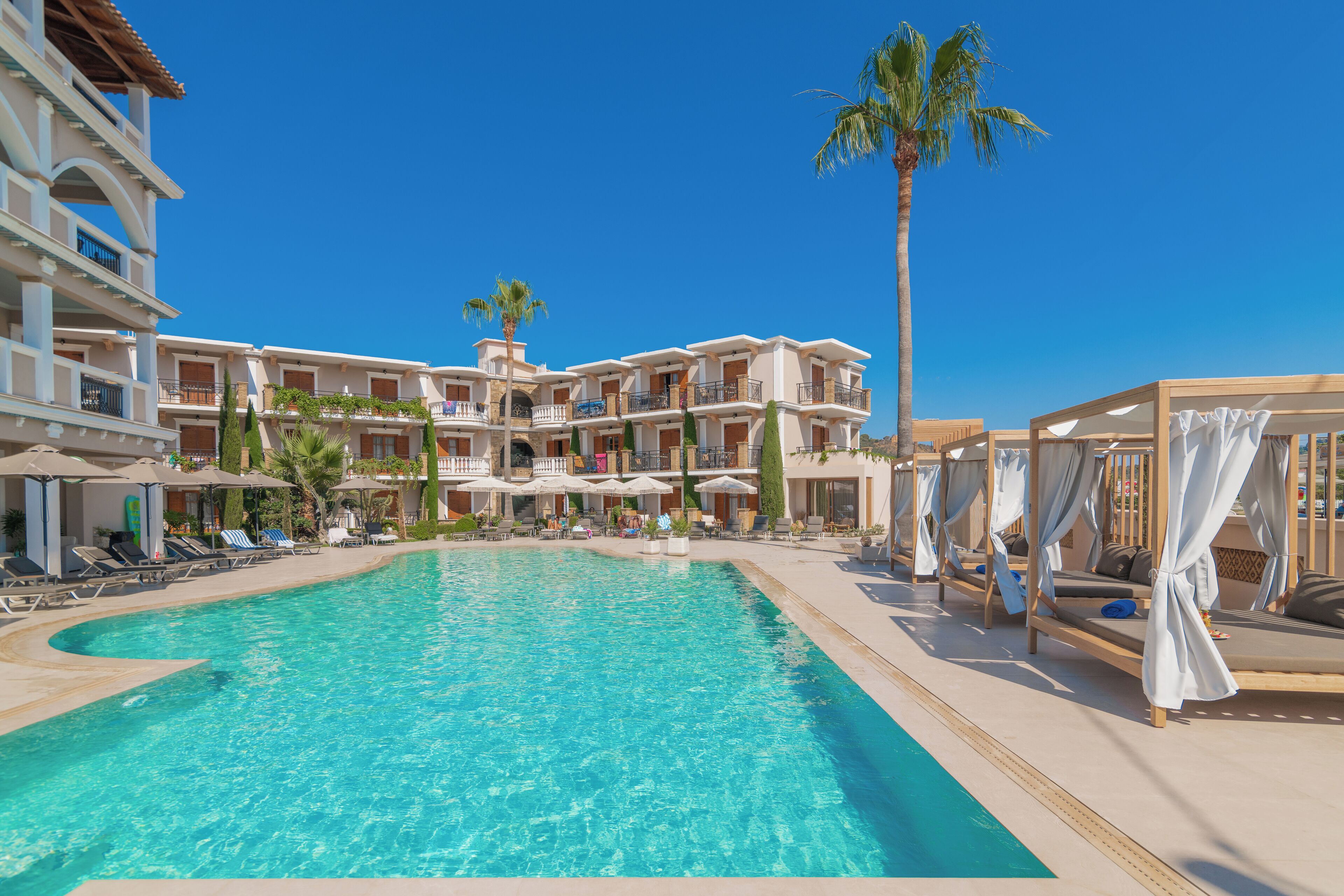 A resort pool area with multiple levels of balconies, sun loungers, and umbrellas.