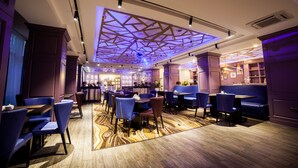 A modern restaurant with a geometric ceiling design, blue upholstered seating, and a patterned carpet. - Absolute Hotel (Astana)