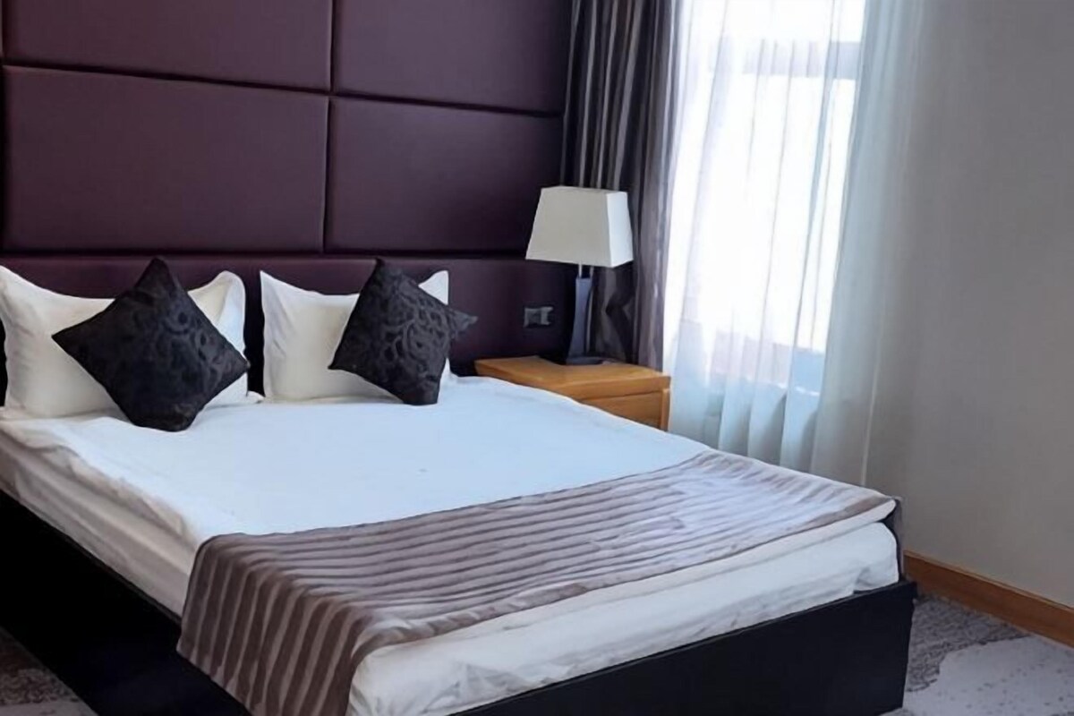 Une chambre d’hôtel avec un grand lit, une table de chevet avec une lampe et une fenêtre avec des rideaux.
