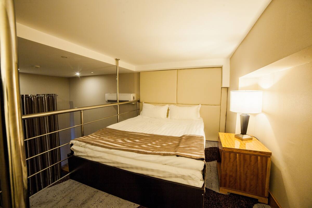 Et hotelværelse med seng, et natbord med lampe, et klædeskab og et spejl på væggen.