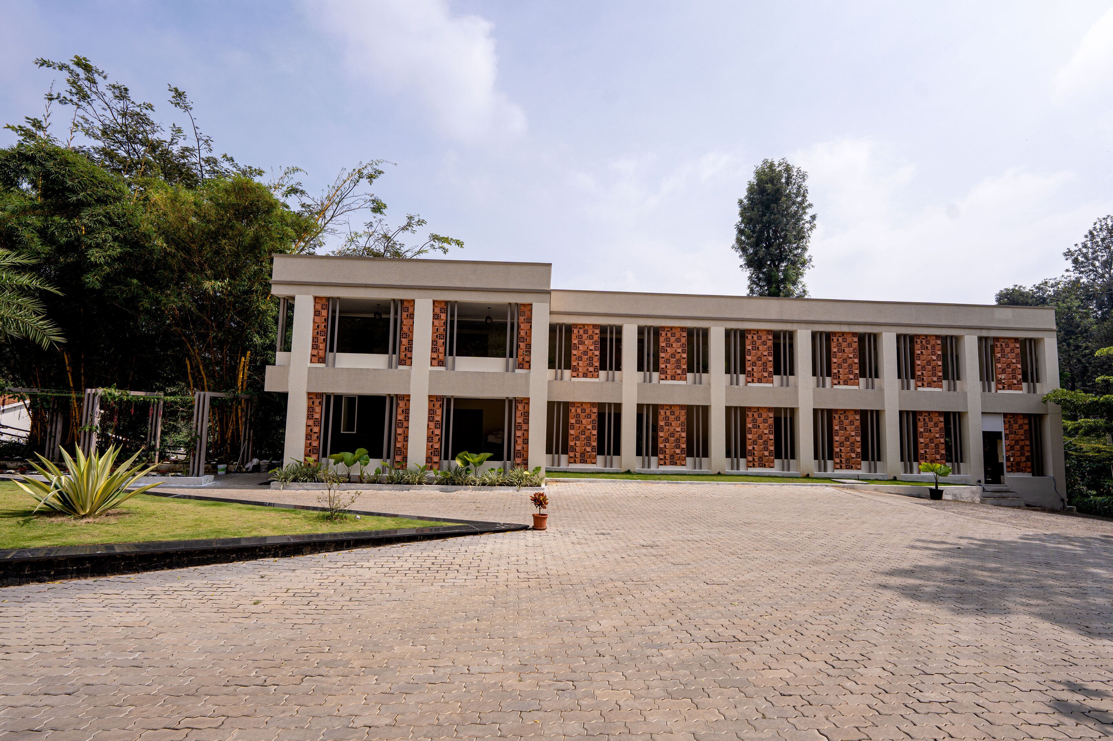 A modern building with a brick facade and large windows, surrounded by a paved courtyard and greenery.