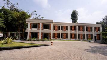 A modern building with a brick facade and large windows, surrounded by a paved courtyard and greenery.