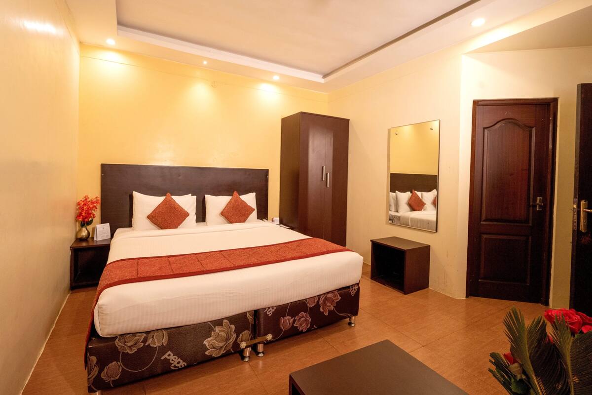 A hotel room with a large bed, a wardrobe, a bedside table, a mirror, and a door.