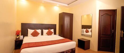 A hotel room with a large bed, a wardrobe, a bedside table, a mirror, and a door.