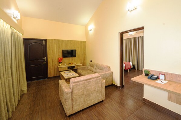 Habitación de hotel con sofá, una pequeña mesa, televisor y mostrador de recepción.