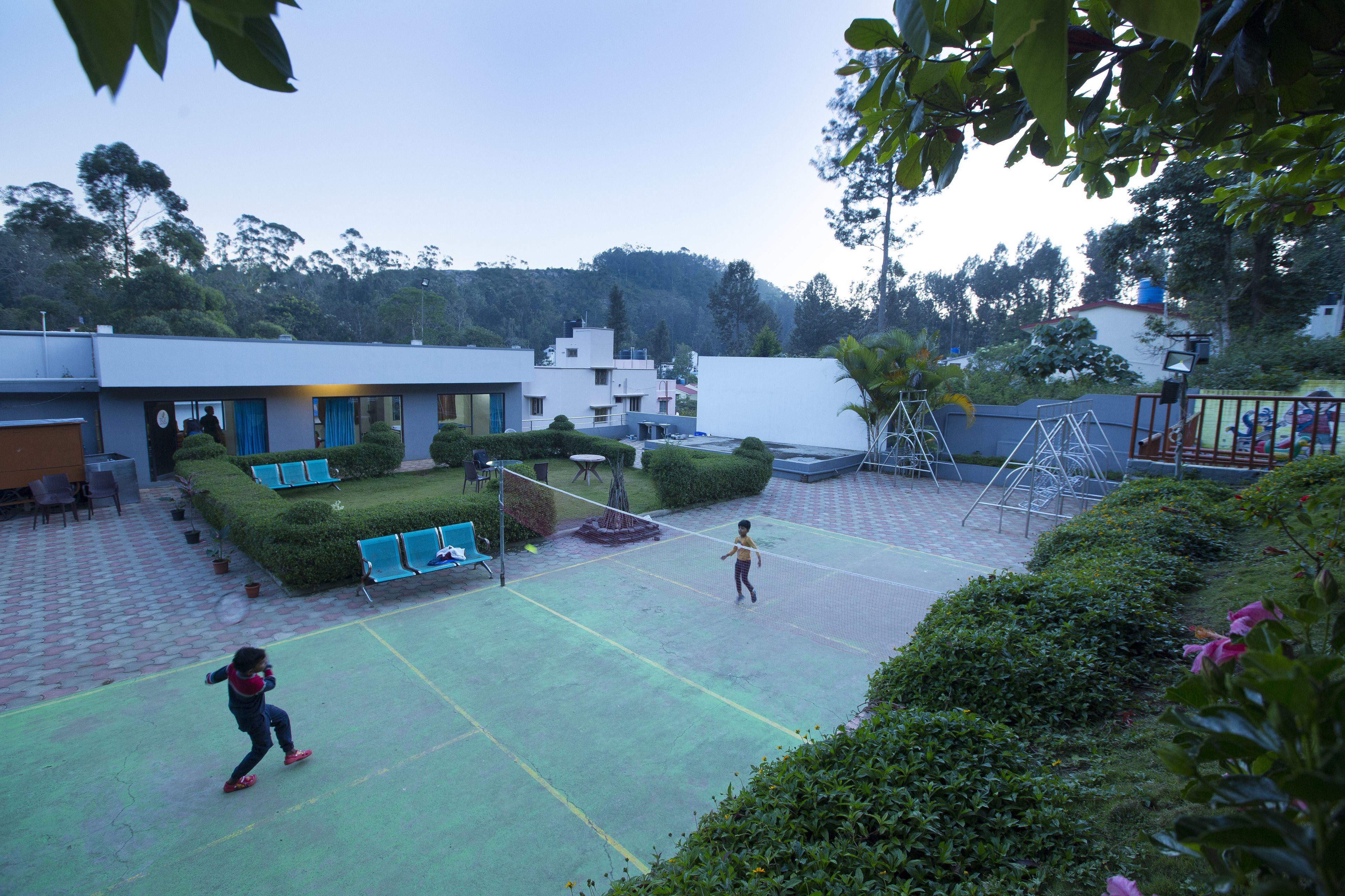 A courtyard with a badminton court, seating areas, and a playground.