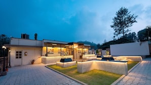 A modern outdoor seating area with a café, a well-maintained lawn, and a paved walkway. - TGI STAR Holidays Yercaud (Yercaud)