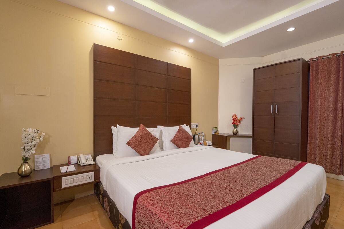 A hotel room with a large bed, a wooden headboard, a nightstand with a phone and a vase of flowers, and a wardrobe.