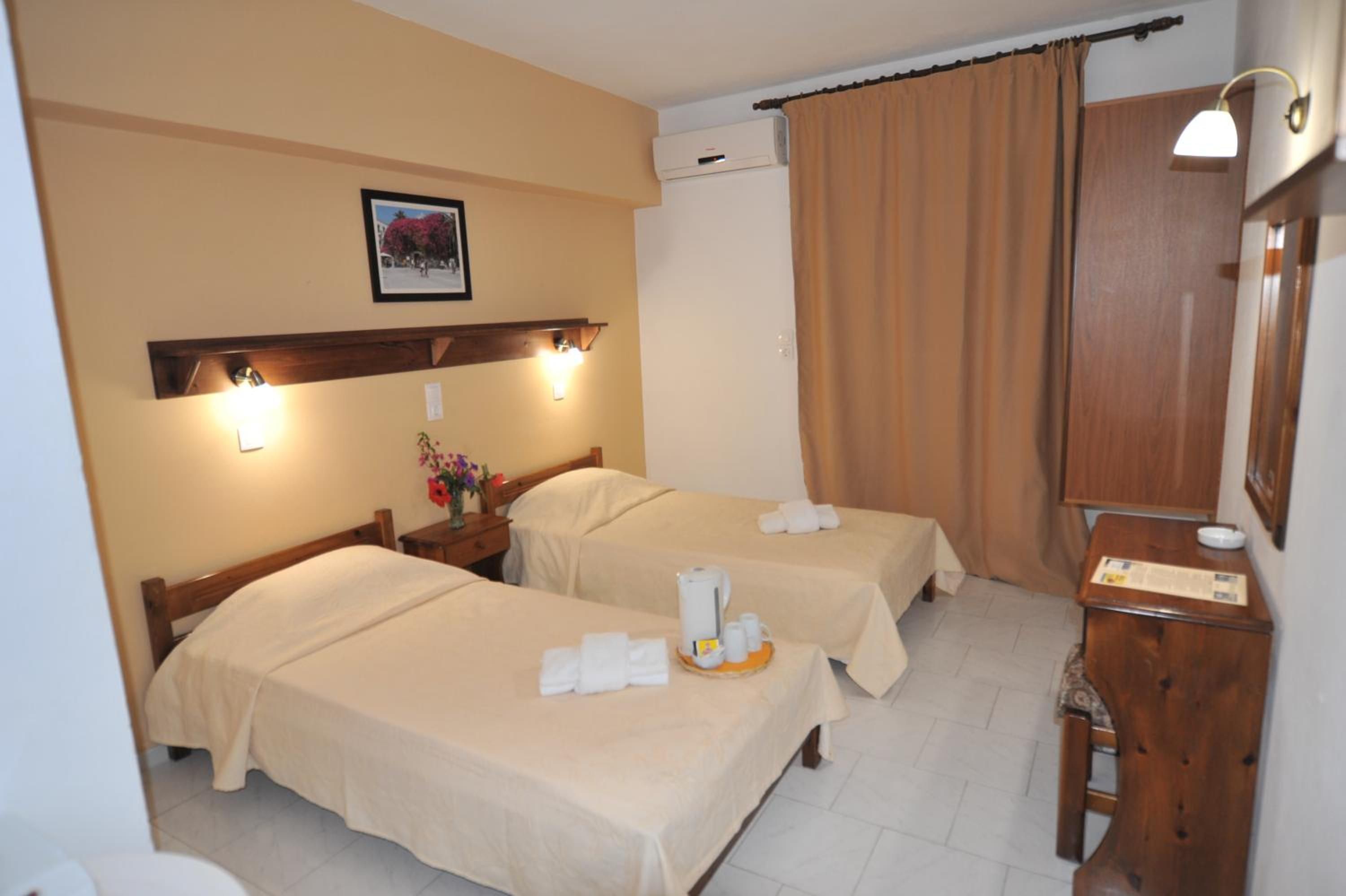 A hotel room with two beds, a wooden nightstand, a desk, and a wall-mounted air conditioner.