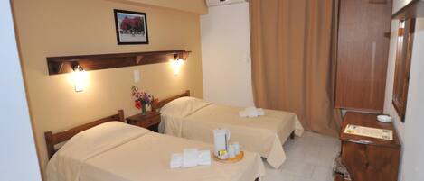 A hotel room with two beds, a wooden nightstand, a desk, and a wall-mounted air conditioner.