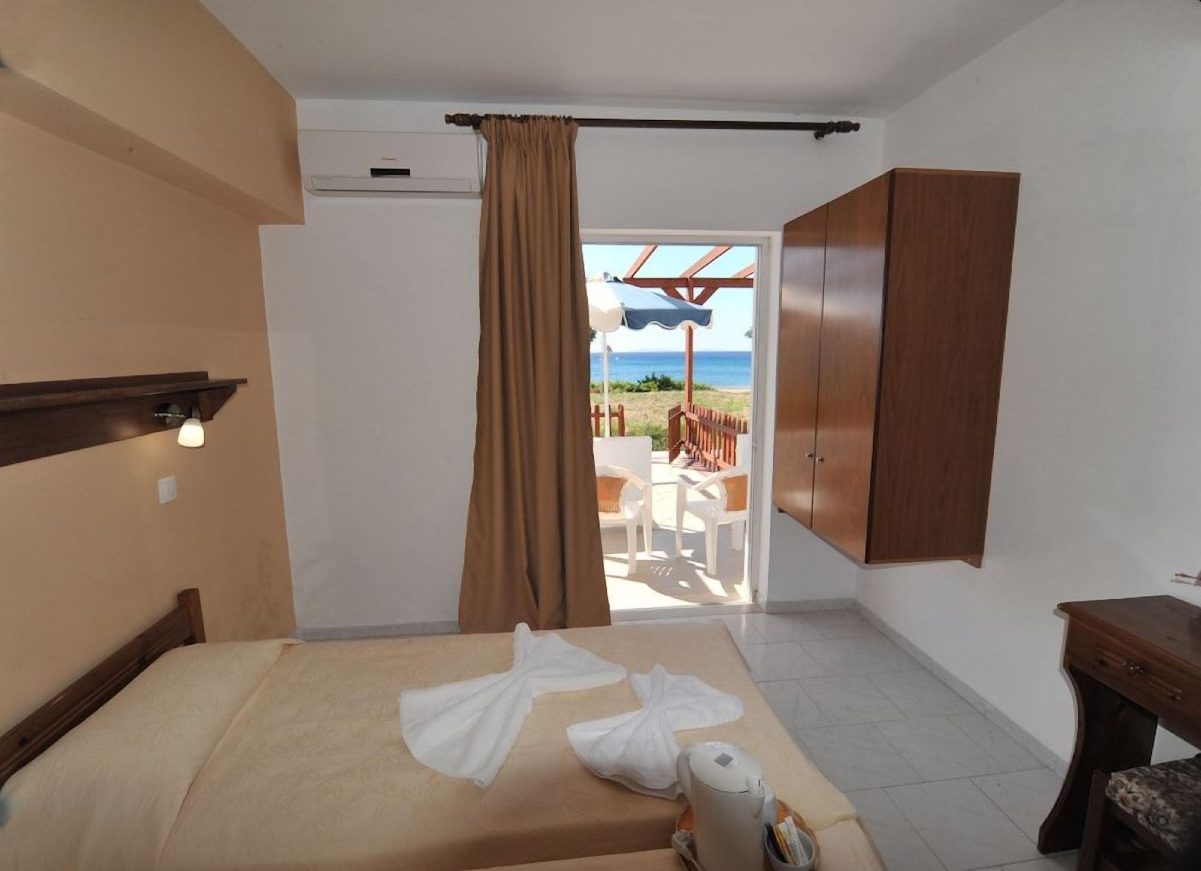 A hotel room with a bed, a wooden wardrobe, a desk, and a view of the beach.