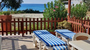 Un patio frente al mar con dos sillones a rayas y una mesa, una valla de madera y vistas al océano.