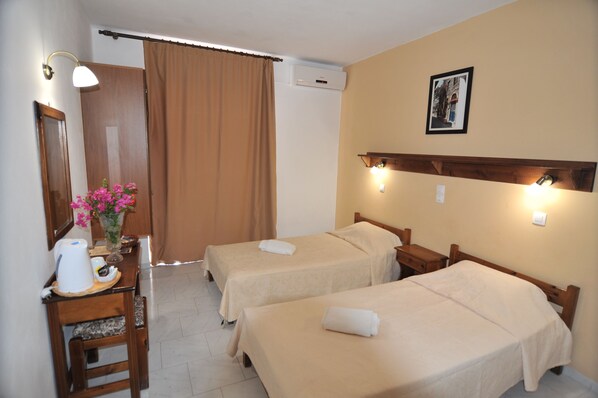 A hotel room with two beds, a wooden desk with a kettle, a vase with flowers, and a picture on the wall. - Irene Studios (Kos)