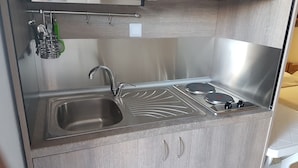 Una cocina compacta con un lavamanos de acero inoxidable, dos hornillas y un mueble pequeño con dos pomos.