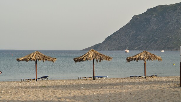 Una playa con tres sombrillas de paja y sillones de descanso.