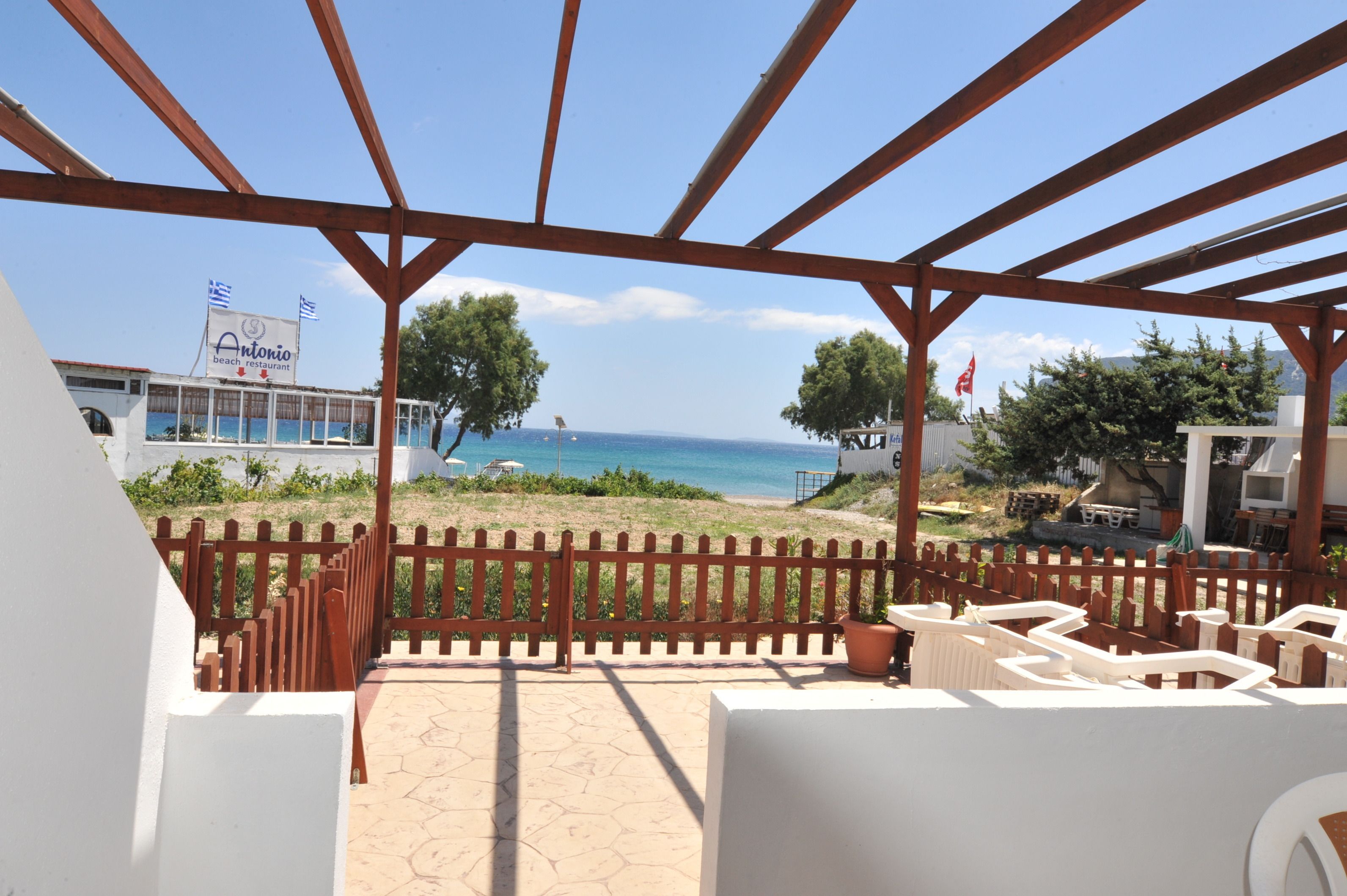 A beachside patio with a view of the sea, a restaurant named Antonio, and a wooden pergola structure.