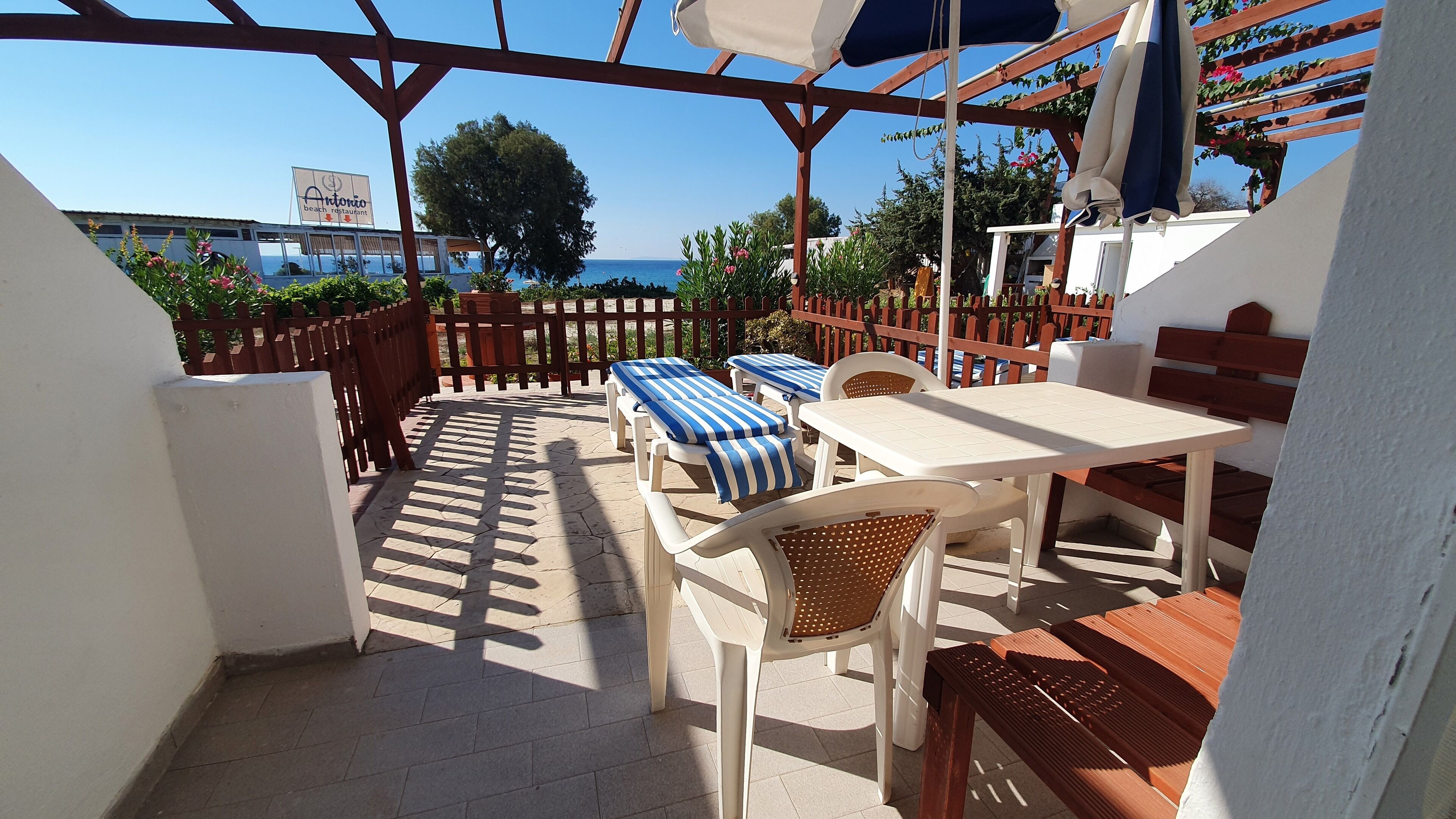A patio area with a table and chairs, a bench, and a view of the sea.