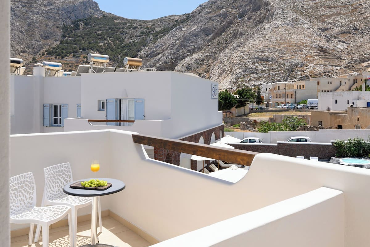A balcony with white chairs and a small table, overlooking a mountainous landscape and a town.