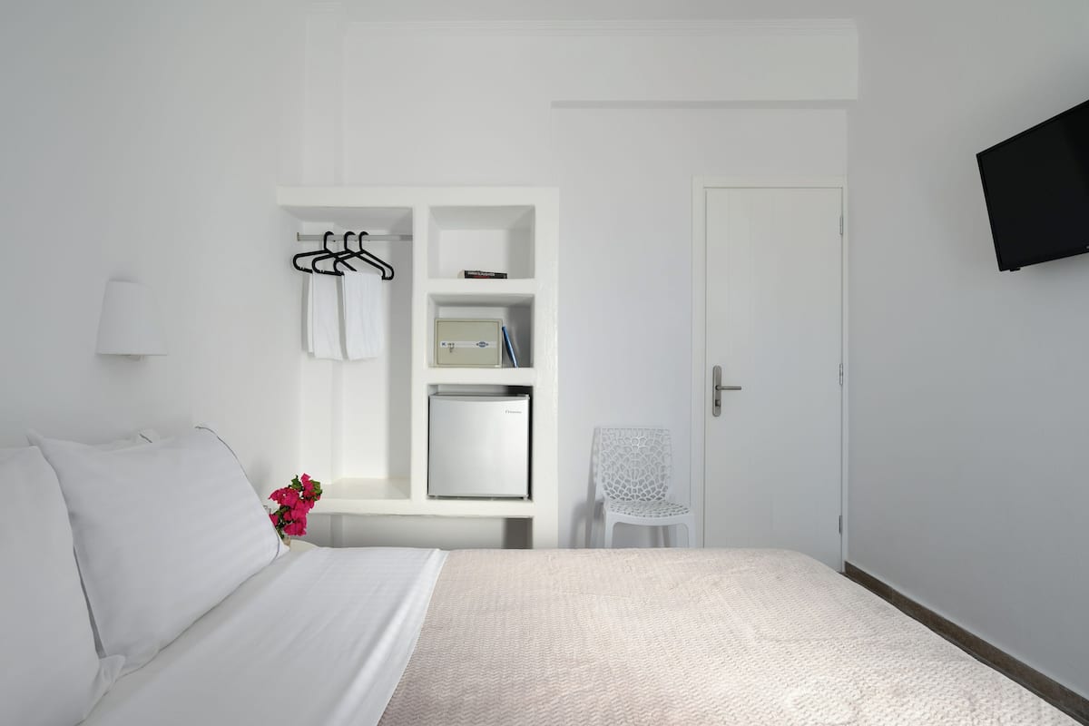 A hotel room with a bed, a desk with a chair, a TV mounted on the wall, and a door.