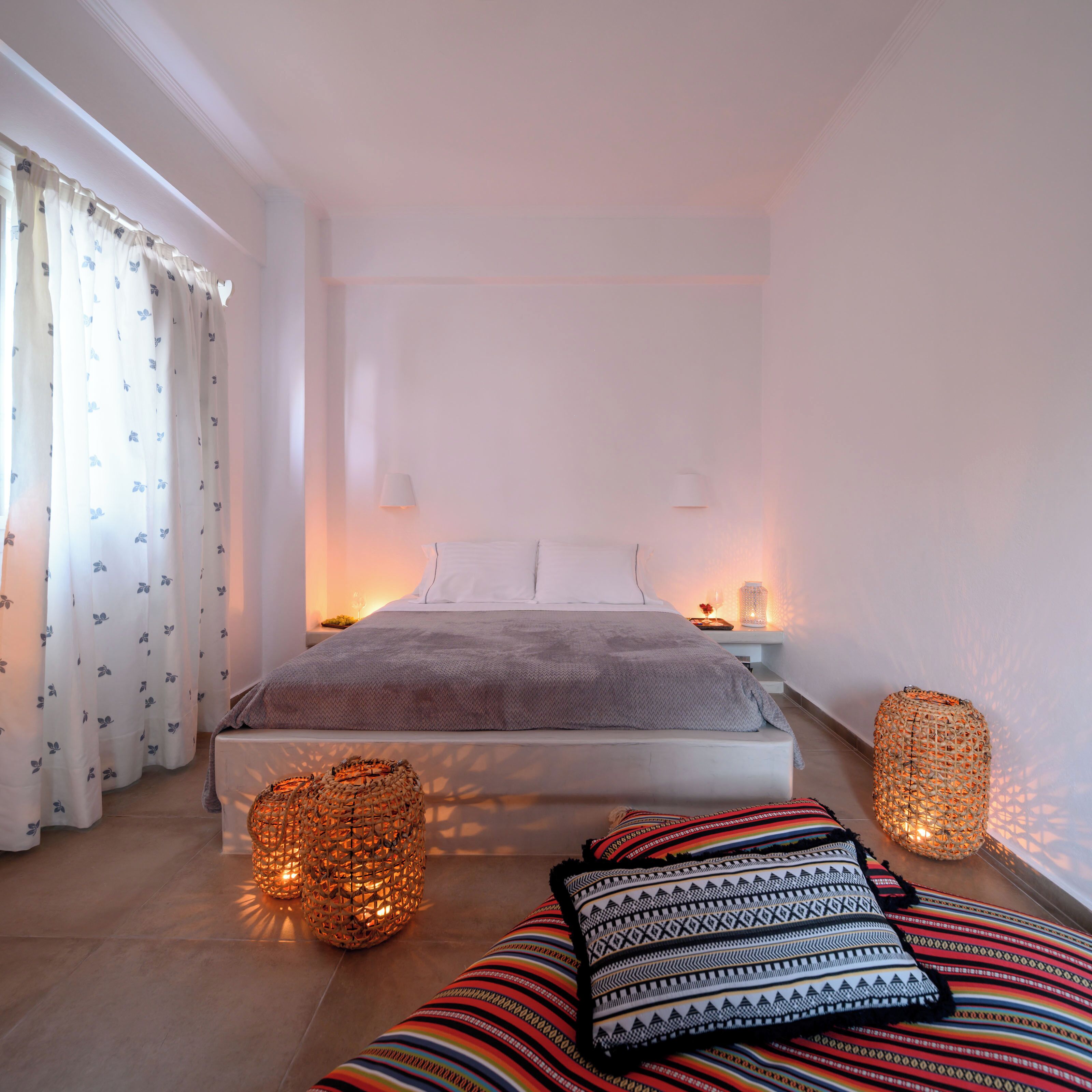 A bedroom with a bed, bedside lamps, a patterned curtain, and a woven basket.