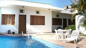 Zona junto a la piscina con pileta, paredes blancas y contraventanas de madera.