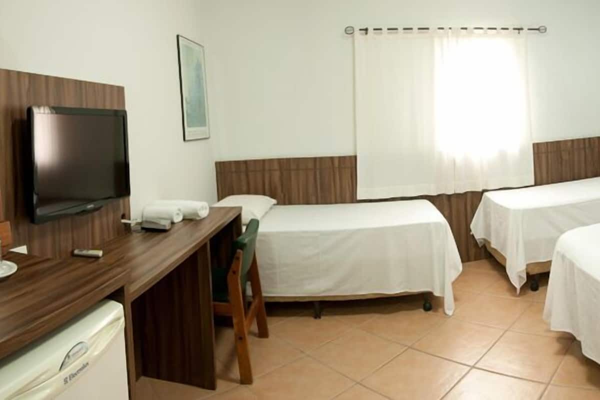 A hotel room with two single beds, a desk with a television, a small table with a chair, and a bathroom with a white toilet.