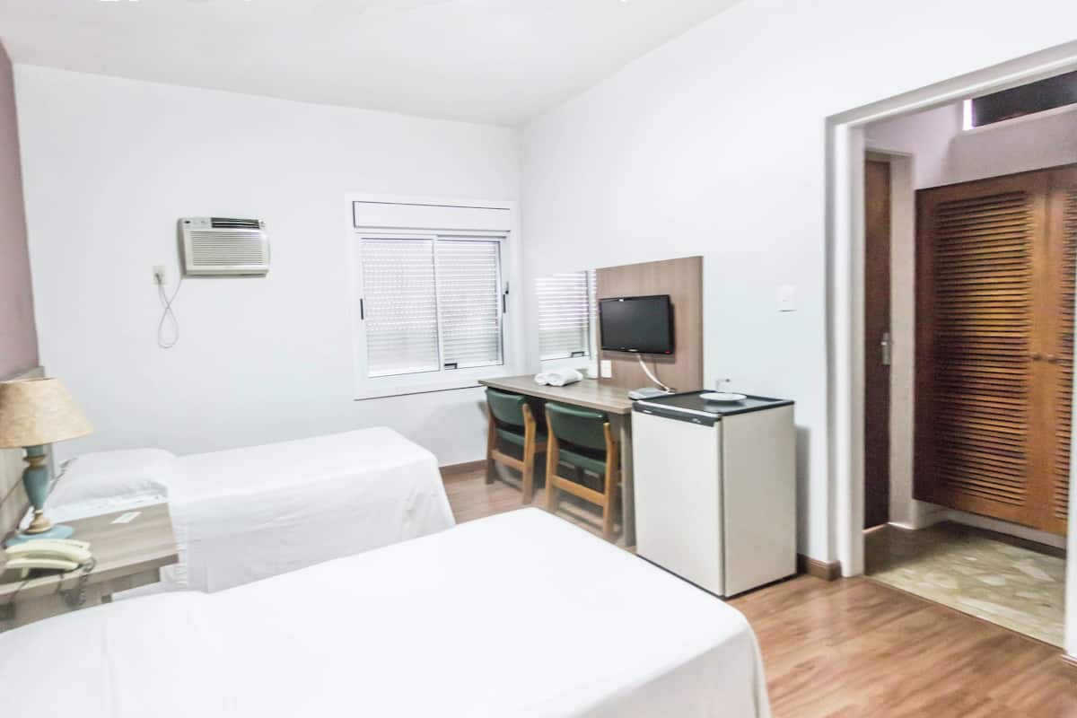 A hotel room with two beds, a desk, a television, an air conditioning unit, and a wooden door.