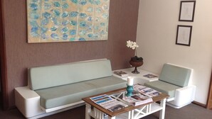 Una sala de estar con un sofá verde claro, una mesa de centro de madera con periódicos y un jarrón decorativo con una orquídea.
