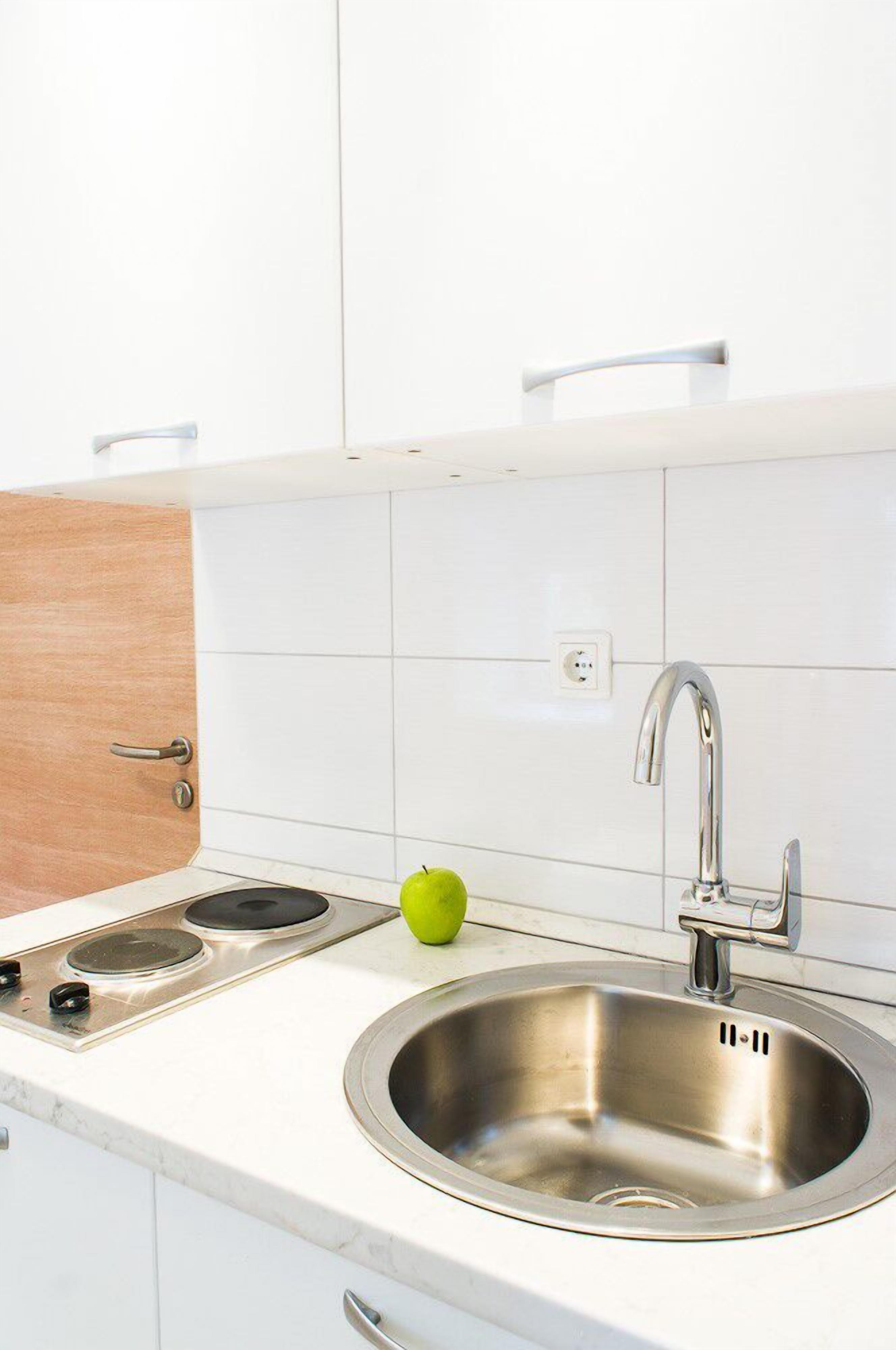 Une cuisine moderne avec des meubles blancs, un évier en acier inoxydable et une seule pomme verte posée sur le plan de travail.