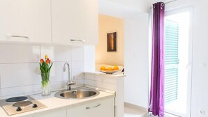 Una cocina moderna con armarios blancos, un lavamanos de acero inoxidable y una pequeña encimera. Hay un jarrón con tulipanes y un cuenco de naranjas sobre la encimera.