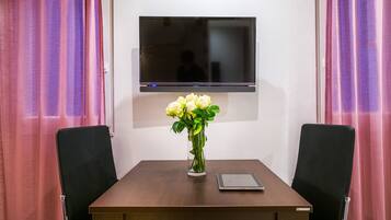Una sala de conferències amb una taula de fusta, dues cadires negres, un vas de vidre amb flors blanques, una tauleta i un televisor de pantalla plana penjat a la paret.