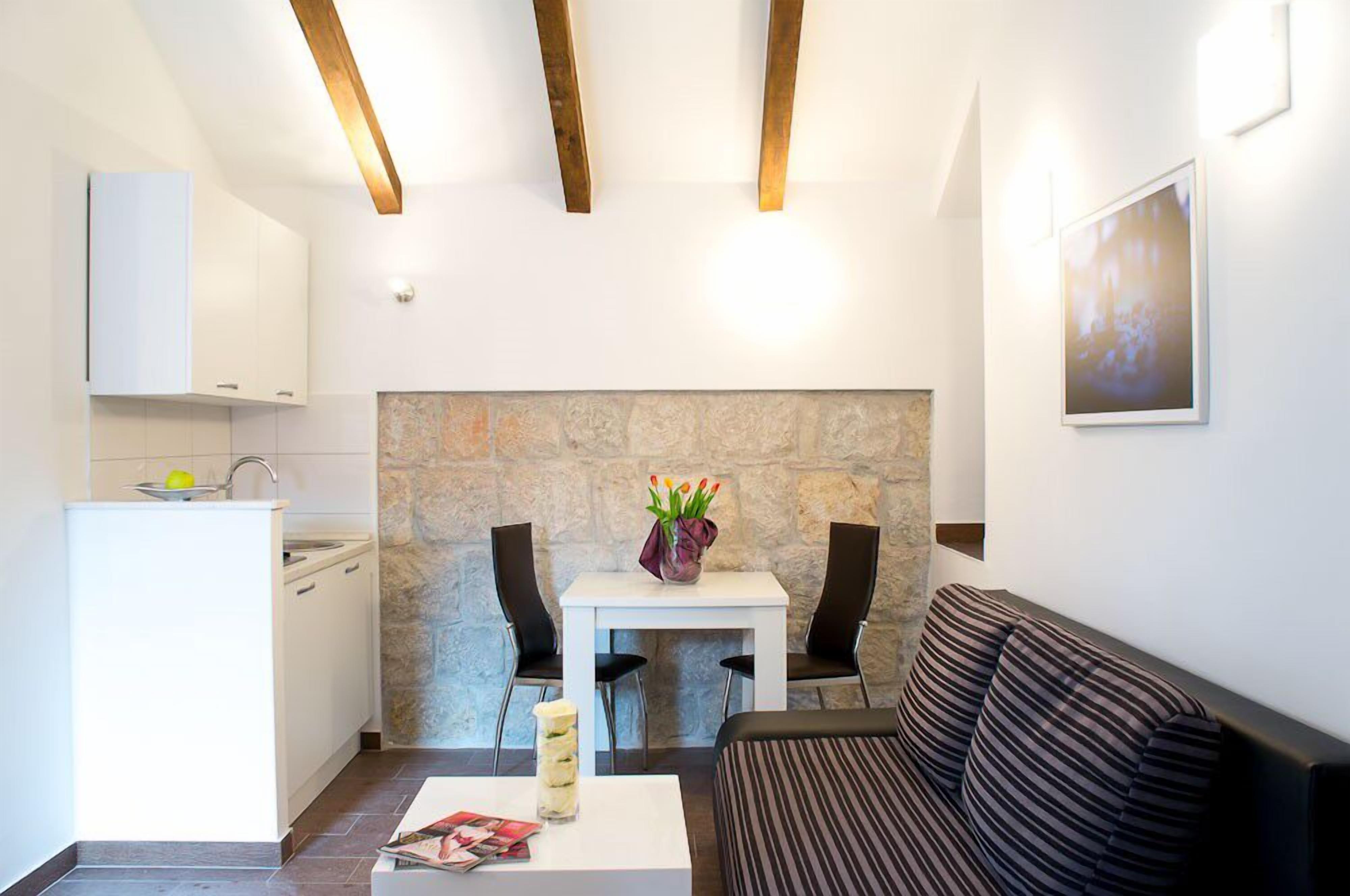 A compact living space with a kitchenette, a dining area with two chairs, a sofa, and a stone accent wall.