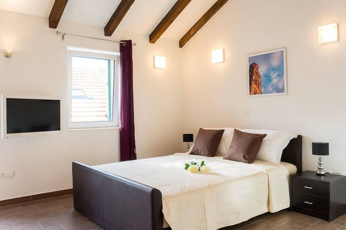A bedroom with a bed, bedside tables, a TV, and a window with curtains.
