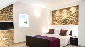 Un dormitorio moderno con una pared de acento de piedra, una cama grande con una manta roja, un televisor de pantalla plana montado en una pared de piedra y una ventana con vistas a zonas verdes.