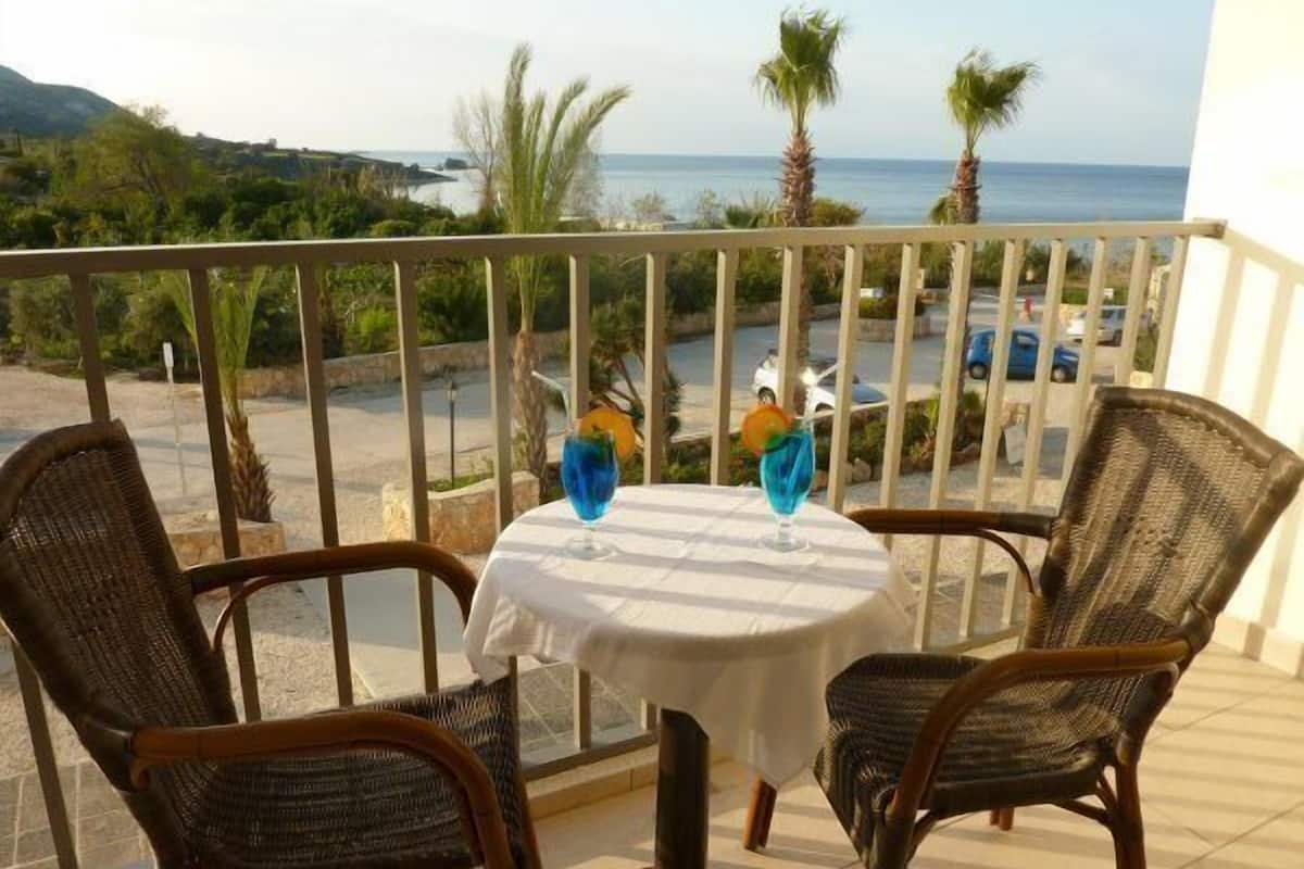 Ein Balkon mit Korbstühlen und einem Tisch, mit Blick auf die Küste, Palmen und einen Parkplatz.